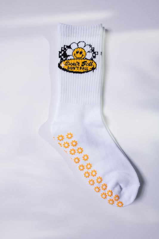 White Pilates grip sock with bright yellow daisy grips and a retro smiley daisy patch.