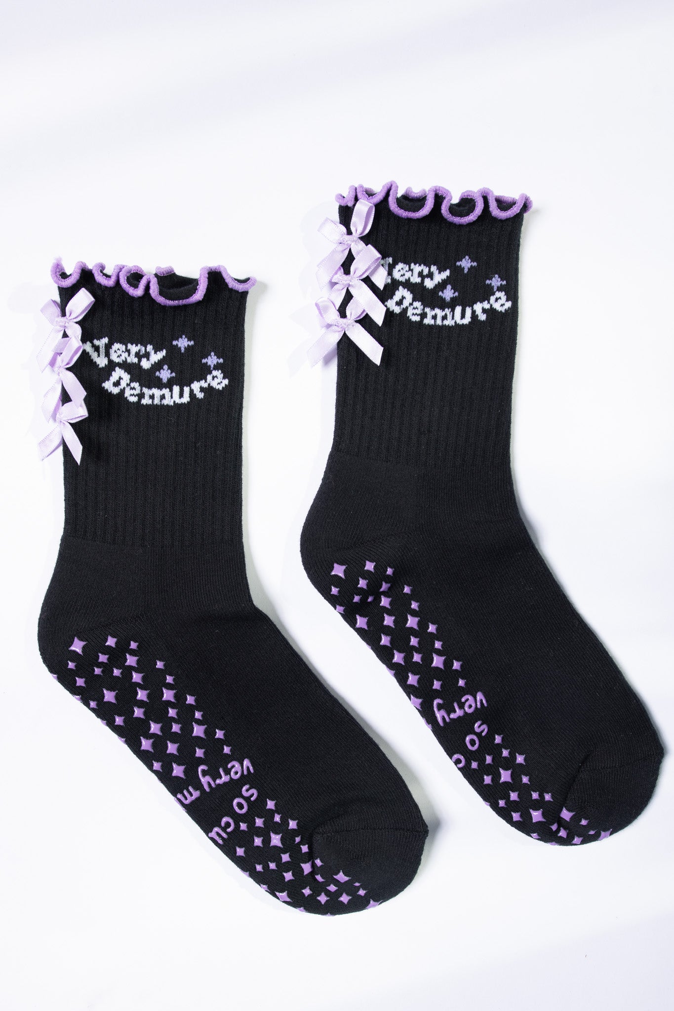 Flat lay of black Pilates socks with lavender text, bows, and non-slip diamond grip pattern.
