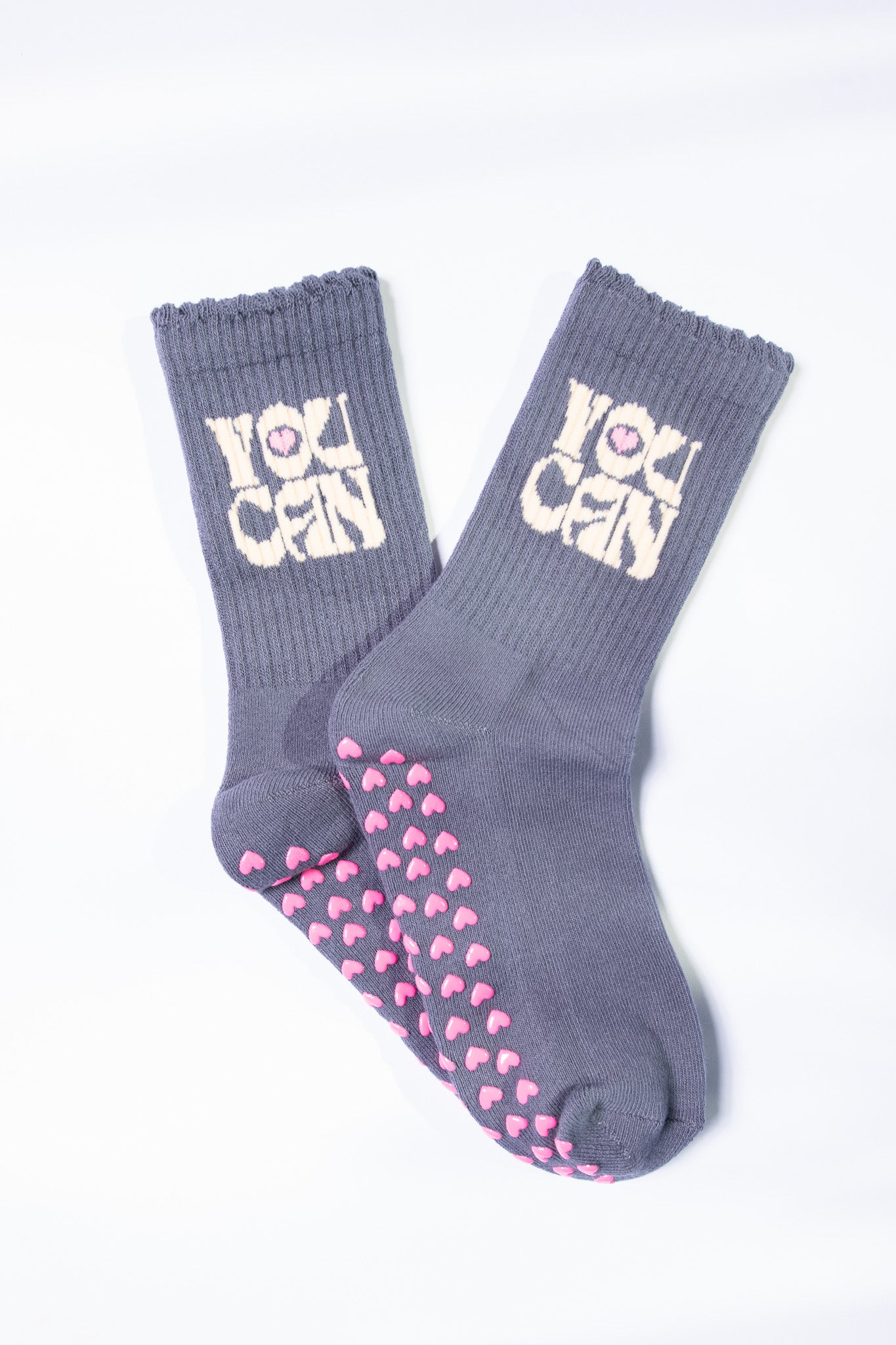 Flat lay of gray Pilates grip socks with cream “YOU CAN” text and pink non-slip heart grips.