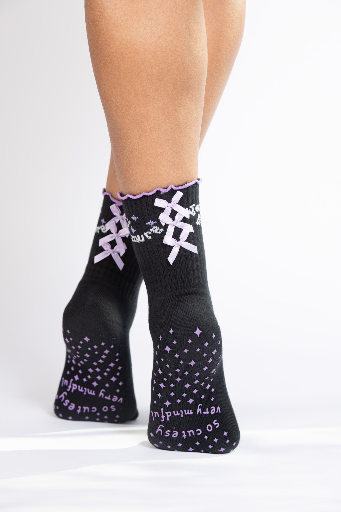 Back view of model wearing black Pilates socks with lavender grip text and decorative ribbon details.