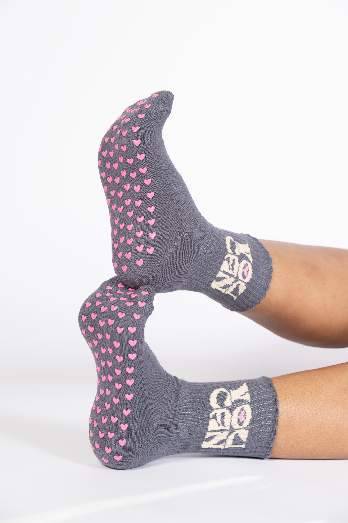 Close-up of pink heart-shaped grips on gray socks with “YOU CAN” text near the ankle in cream lettering.
