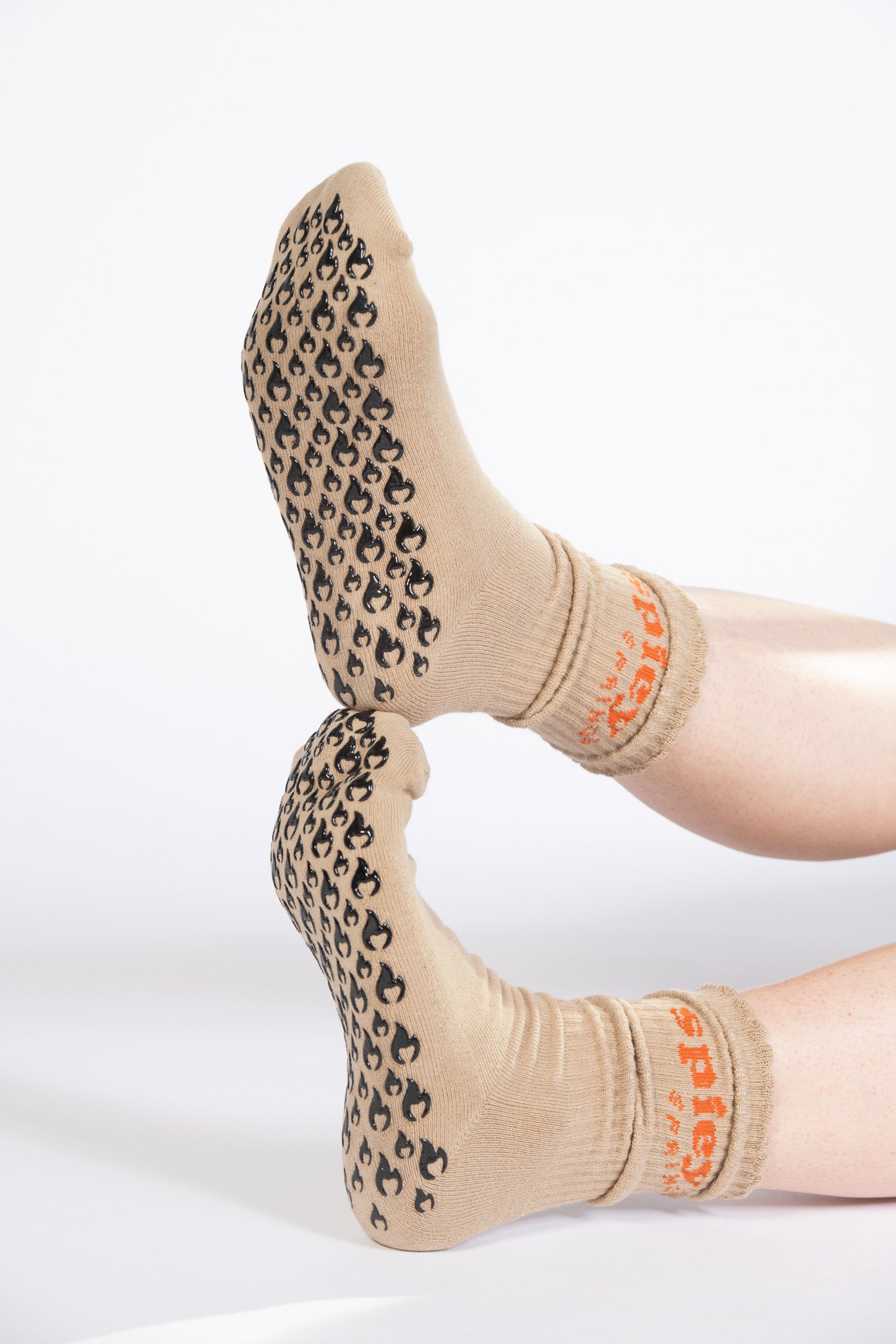 Close-up of flame-shaped non-slip grips on tan Pilates socks with scrunched cuffs and “spicy springs” text.