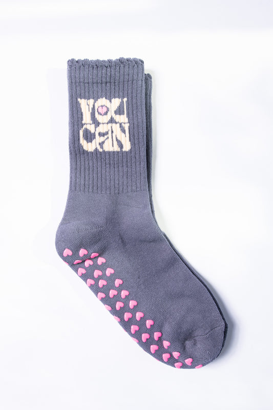Flat lay of gray Pilates sock with “YOU CAN” embroidered in cream block letters and pink heart grips on sole.