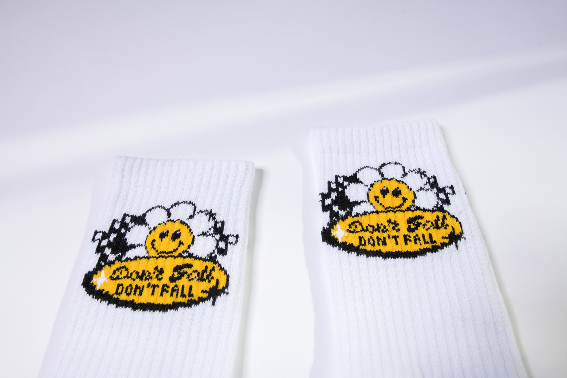 Close-up of retro daisy patch with smiley face and “Don’t Fall” message on white Dew Health & Wellness Pilates socks. Checkerboard flags add a playful touch.
